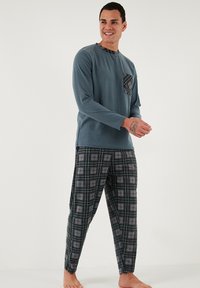 Férfi pizsama szett, amely tartalmaz egy egyszínű, kék, hosszú ujjú felsőt kockás zsebbel és fekete kockás nadrágot, texturált anyaggal, világosszürke mintákkal.