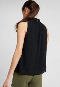 Blusa nera senza maniche con colletto alto, vestibilità ampia e dettaglio con bottone sul retro. Realizzata in tessuto leggero e morbido.