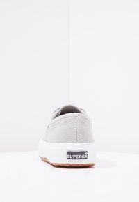 Szare płócienne sneakersy z białą gumową podeszwą, charakteryzujące się teksturowanym wzorem i czarnym logo "SUPERGA" na pięcie.