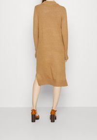 Stickad klänning i ullblandning i camel-färg, med långa ärmar, krage och sidoklipp i fållen. Bärs med bruna platåklackar.