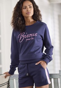 Marineblaues Sweatshirt mit "Bisous pour toi" in pinker Schrift; kombiniert mit passenden Shorts mit seitlichen Streifen. Weicher Stoff, lässiger Schnitt.