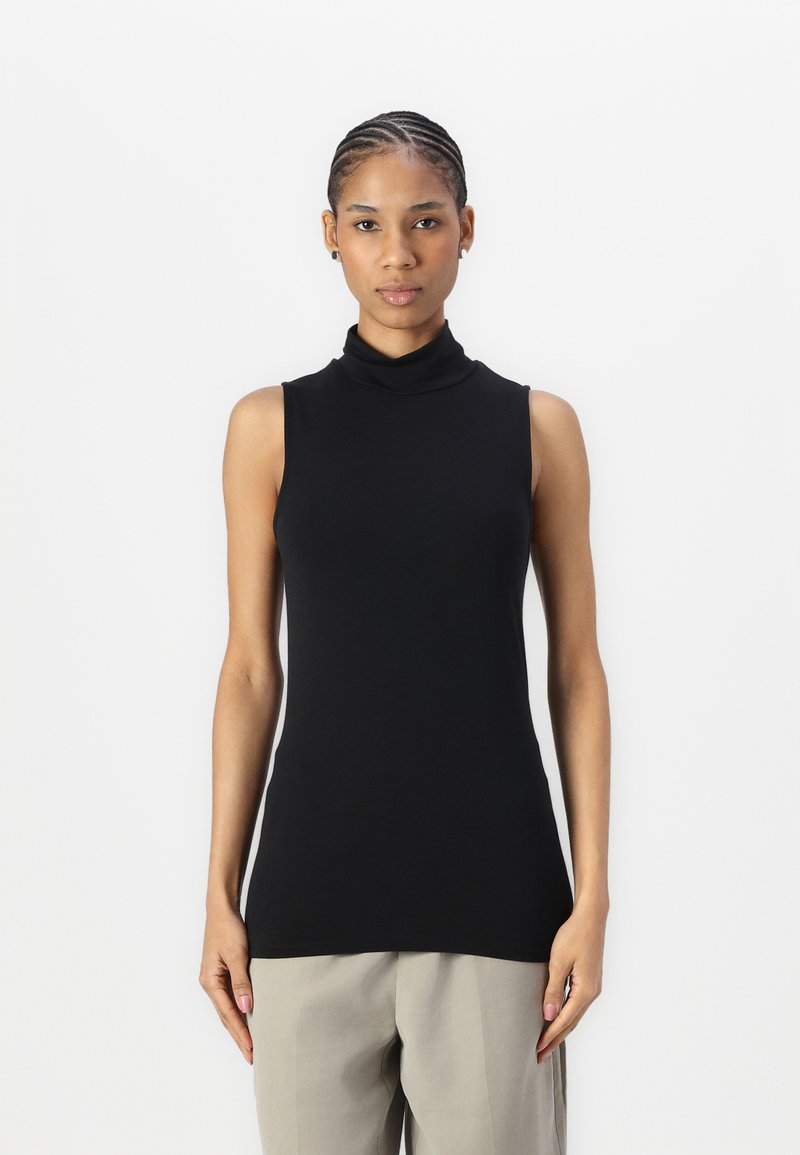 Haut sans manches en turtleneck noir en tissu doux et extensible ; design ajusté avec un col haut, associé à un pantalon beige clair.