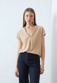 Beige t-shirt met korte mouwen en een V-hals, voorzien van een subtiele textuur, gecombineerd met donkerblauwe hoge taille broeken. Minimalistisch ontwerp en een relaxte pasvorm.