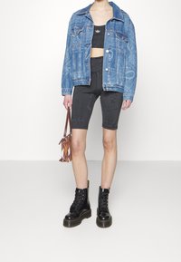 Džínová bunda, černý vzorovaný crop top, černé cyklistické šortky, černé šněrovací boty a hnědá vzorovaná kabelka.