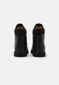 Bottes en cuir noir avec un petit talon, un col de cheville rembourré et une doublure contrastante en tan. Présente des détails de couture et une semelle en caoutchouc.