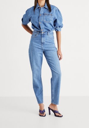 Denimskjorte med knaplukning, korte pufærmer og en brystlomme. Højttaljede blå jeans med lige ben, kombineret med lilla hæle.