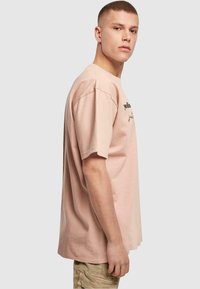 Lyserød bomulds t-shirt med korte ærmer, afslappet pasform, med sort tekstgrafik på fronten. Enkel design uden yderligere mønstre.