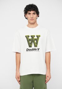 T-shirt de algodão branca com um logo "W" verde texturizado e texto "Double A" preto. Corte largo com mangas curtas. Design simples e moderno.