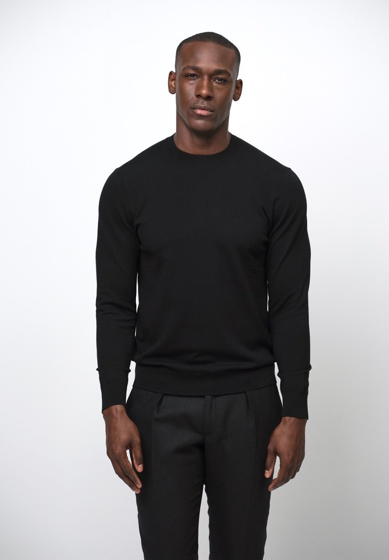 Svart långärmad tröja i ett slätt stickat tyg med en åtsittande design. Muddarna och nederkanten är ribbade för extra textur.
