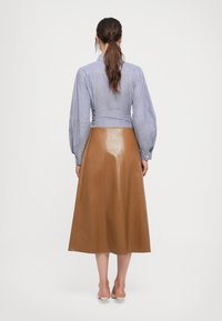 Camisa de botones a rayas con mangas abullonadas combinada con una falda midi de cuero marrón. Textura suave y forma A, hasta la rodilla.