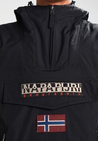 Černá mikina s vysokým límcem, obsahující zip, logovou nášivku a červeno-modrou norskou vlajku. Texturovaná vnější tkanina.