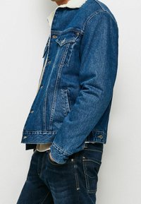 Jeansjacka i mörkblått med en vit, fluffig krage. Har två bröstfickor, knäppningar och en avslappnad passform. Texturerat material.