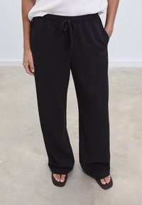 Zwarte, lichte, elastiche taillebroek met zijzakken, losse pasvorm en trekkoorddetail. Glad materiaal en rechte pijpdesign.