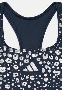 Marine blsports-bh med et sølv leopardprintmønster, der har racerback-design og et Adidas-logo på forsiden.