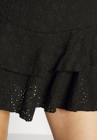 Jupe noire avec un design à couches, un motif à œillets floraux, un tissu texturé et un ourlet volanté.