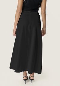 Zwarte maxi rok met een gladde textuur, vloeiende ontwerp en een elastische tailleband. Draag het met zwarte sandalen met hoge hakken.