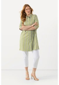 Camicia a righe verde e bianca con colletto, maniche corte e taglio dritto, abbinata a pantaloni bianchi alla caviglia e tacchi dorati.