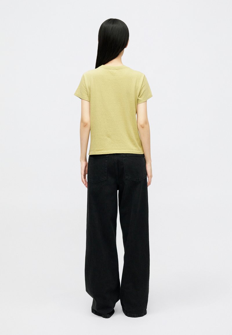 Olivgrön bomulls-t-shirt med rund halsringning, kombinerad med högmidjade svarta vida byxor med bakfickor och en avslappnad passform.