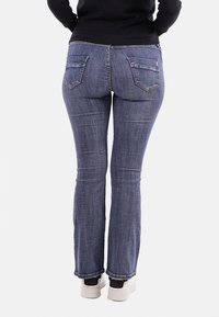 Jeans a zampa d'elefante in denim blu con due tasche posteriori, una texture liscia e leggera sbiaditura. Indossati con sneaker bianche.