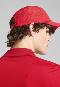 Gorra roja con diseño perforado y correa ajustable, combinada con una camisa roja de cuello a juego, que muestra una textura suave y un estilo ajustado.