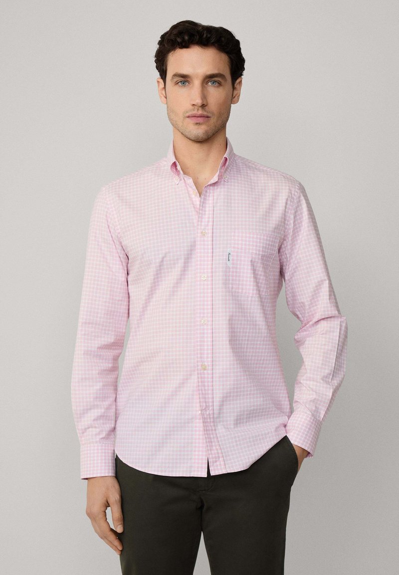 Camisa de cuadros rosa de manga larga con cuello abotonado, bolsillo frontal y sutil marca. La tela parece suave con una textura ligera.