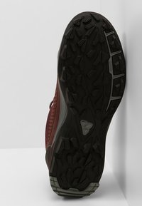 Röd vandringssko med en texturerad ovandel, som har ett ventilerande mesh, gummisula med mångriktade greppknoppar och förstärkt tåhätta.