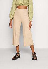 Pantalons culotte beige à rayures avec taille haute, associés à un blouse cropped vert olive et des sandales noires à lanières avec des accents en métal argenté.