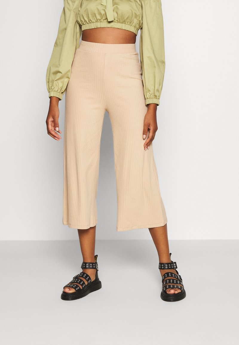 Pantalons culotte beige à rayures avec taille haute, associés à un blouse cropped vert olive et des sandales noires à lanières avec des accents en métal argenté.
