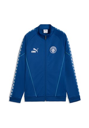 Veste de sport Puma bleue avec fermeture éclair intégrale, logo Manchester City sur la poitrine, logo Puma blanc et texte "KING", rayures à motifs sur les manches et passepoil bleu clair.
