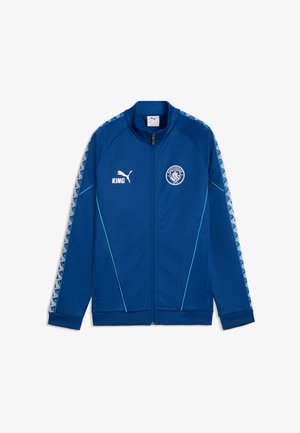 Blaue Puma-Sportjacke mit durchgehendem Reißverschluss, Manchester City-Logo auf der Brust, weißem Puma-Logo und Text "KING", gemusterten Streifen an den Ärmeln und hellblauen Paspeln.