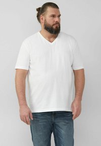 Weißes T-Shirt mit V-Ausschnitt aus Baumwolle, kurzärmlig, lässiger Schnitt. Kombiniert mit blauen Jeans. Einfaches Design, keine sichtbaren Muster.