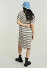 Pasiasta sukienka z krótkim rękawem, o luźnym kroju, długości do kolan i z bocznymi rozcięciami. Noszona z niebieskim kapeluszem typu bucket i masywnymi czarnymi butami.