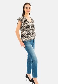 Top a righe bianco e nere con maniche arricciate, abbinato a jeans azzurri chiari e tacchi alti neri. Taglio semplice e moderno.