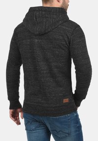 Dark gray sweatshirt with a textured, heathered appearance. Features a hood, long sleeves, and a small leather accent near the hem.
