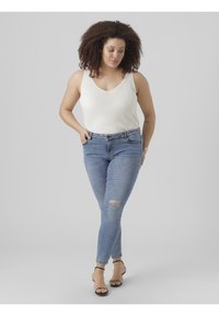White ribbed tank top paired with light blue skinny jeans featuring a knee rip. Model wears black ankle strap sandals, with a neutral background.