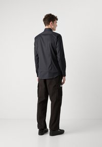Camisa oscura con un diseño ajustado, de mangas largas y cuello puntiagudo. Combinada con pantalones cargo negros que cuentan con bolsillos laterales y un corte holgado.