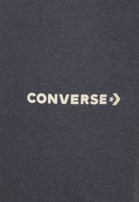 Tengerészkék anyag sima felülettel, rajta a "CONVERSE" szó fehér betűkkel, egy csillag és nyíl grafika kíséretében.