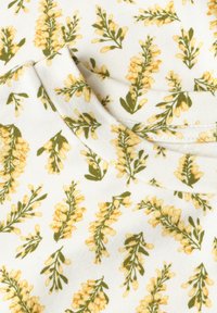 Tissu blanc avec un motif de petits bouquets de fleurs jaunes et de feuilles vertes, montrant un bord plié et un détail de couture.