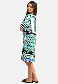 Luftiges Kleid mit einer Mischung aus geometrischen Mustern in Blau, Grün, Schwarz und Weiß. Weicher Stoff, kurze Ärmel und knielang.