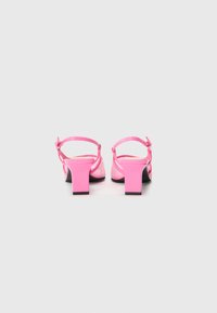 Sandalias de tacón rosa con tacón bloque, tira en el tobillo y detalles decorativos. Acabado suave con un diseño texturizado en la parte superior.