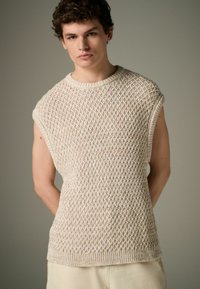 Pull sans manches en tricot beige avec un motif en losanges texturé, col rond et ourlet côtelé. Design léger et légèrement ample.