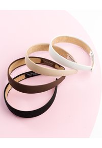 Fire forskellige stofindtrukne hårbånd i sort, brun, beige og hvid arrangeret på en pink og hvid overflade.