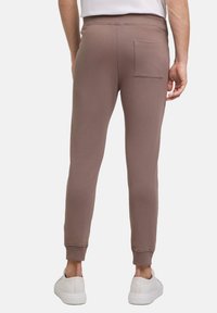 Braune, figurbetonte Jogginghose aus weichem Material mit einer Gesäßtasche und gerippten Bündchen am Knöchel, kombiniert mit weißen Sneakers.