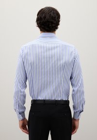 Camicia a righe in azzurro chiaro e bianco, maniche lunghe, polsini abbottonati, colletto classico, indossata con pantaloni neri, vista da dietro.