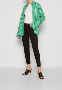 Grön- och vitrandig skjorta med knappar, svarta figurnära byxor och svarta öppna klackar. Slät tyg, skräddarsydd passform, långa ärmar.