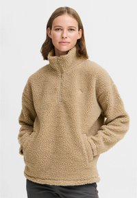Pull-over en polaire beige avec un col montant, fermeture éclair quart de tour, et poches latérales. Tissu texturé et doux avec des poignets et un ourlet élastiques.