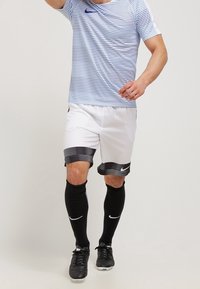 Pantalones cortos de fútbol blancos con rayas horizontales negras, combinados con una camiseta a rayas azul y blanca. Medias negras hasta la rodilla y botas de fútbol negras.