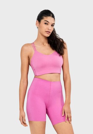 Top de sport court ajusté rose à fines bretelles, associé à un short taille haute assorti. Tissu lisse et extensible pour flexibilité et confort.