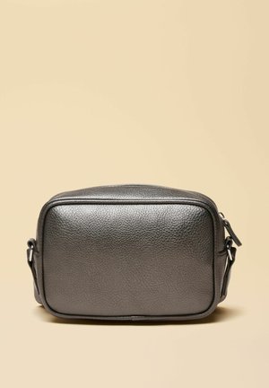 Kleine rechteckige schwarze Umhängetasche aus strukturiertem Leder mit verstellbarem Riemen und Reißverschluss, vor einem beigen Hintergrund.