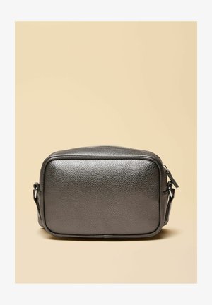 Kleine rechteckige schwarze Umhängetasche aus strukturiertem Leder mit verstellbarem Riemen und Reißverschluss, vor einem beigen Hintergrund.